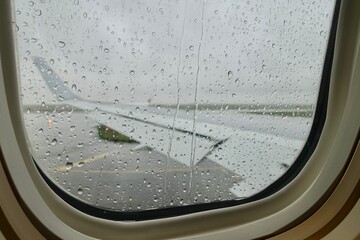滴の付いた飛行機の窓から見る翼と空港