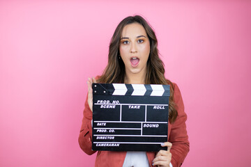 Young beautiful woman wearing casual jacket over isolated pink background holding clapperboard very...