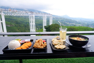 serving dishes of chicken katsu, crispy mushrooms and Javanese noodles with natural views