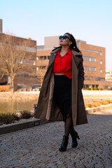 Stylish woman in red blouse with trench coat in urban setting.
