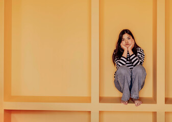 Asian girl sits within geometric structure, her pose indicating a sense of restriction or...