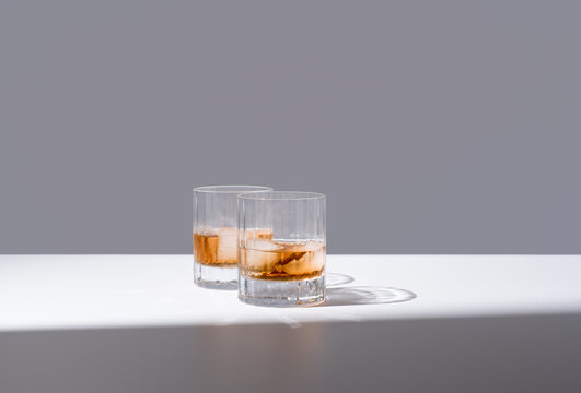 Dos vasos de whisky escocés con hielo sobre fondo gris