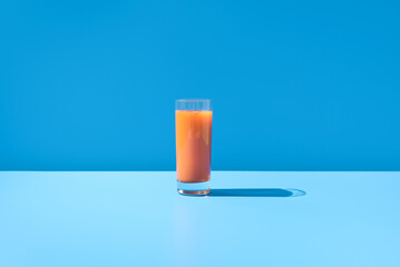 Jugo de zanahoria en un vaso transparente sobre fondo azul