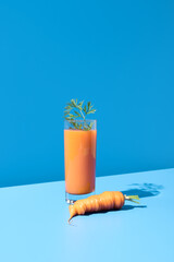 Jugo de zanahoria adornado con hojas verdes en un vaso transparente sobre fondo azul	
