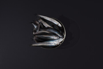 Anchoas frescas dentro de un recipiente trasparente sobre fondo negro. Vista superior