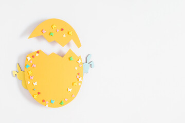 Easter decor concept. Frame made in shape of an Easter egg with colorful Easter eggs and sugar sprinkled candies on white background. Top view. Flat lay.