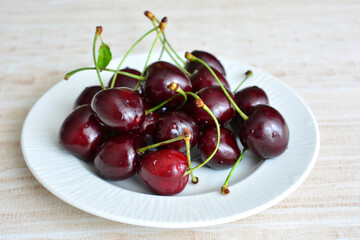 a plate of cherries with a green stems close up  