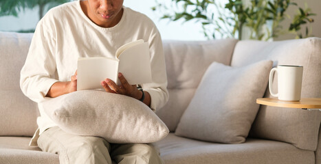Cropped shot of millennial man sitting on a comfortable couch enjoying a good book with a smile of...