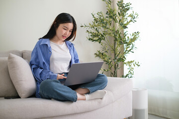 Smiling young woman freelancer sitting on couch and using laptop, remote work or studying online.