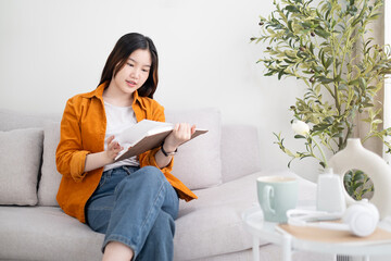 Calm young woman sitting on comfortable sofa at home and reading book.