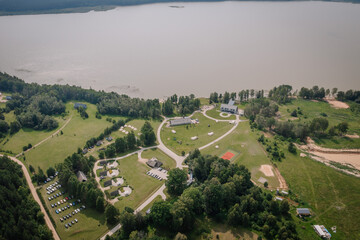 Dobele, Latvia - August 18, 2023 - Aerial view of a rural landscape with buildings, tents, a parking area, and a body of water.