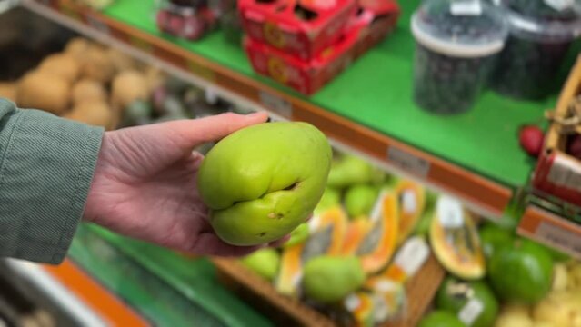 A shopper shows a fresh chayote in his hand against a backdrop of food shelves in a supermarket.