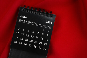 June 2024 Black spiral desktop calendar on red textile.