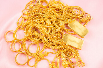 Many gold necklaces and gold bars on pink cloth background.