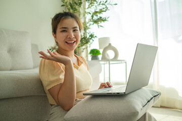 Cheerful young woman using laptop on floor in living room.