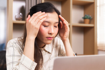 Young Asian stressed women in casual overworked using laptop working at home in living room,...