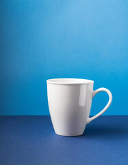 Obraz premium Close-up of ceramic white cup on isolated blue background. Tea or coffee mug. Drink ware. Mock up.