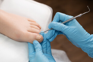 Pedicure master uses nail instrument while toe nails treatment.
