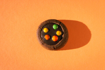 Brown cookie with colourful drops on peach fuzz baclground. Chocolate biscuit in sunlight on orange...