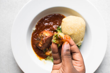 Overhead view of Nigerian okro and stew with eba in a hand, top view of okro soup and eba