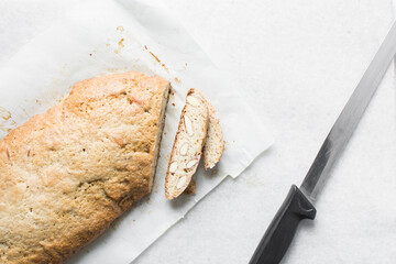 slicing almond biscotti on white parchment lined tray, almond cantucci cookies on a white chopping...