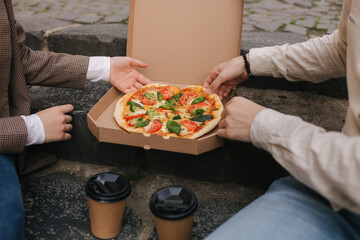 Close-up of Couple grab slices of pizza from box at the outdoor. Man and woman hands taking pizza....