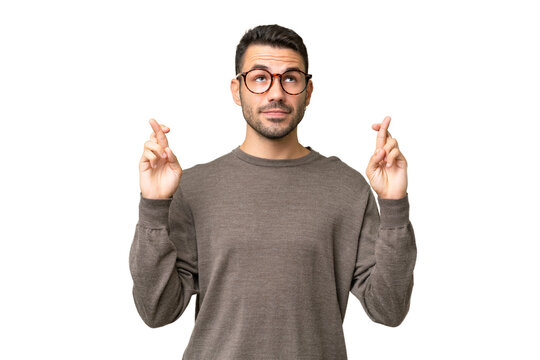 Young handsome caucasian man over isolated background with fingers crossing and wishing the best