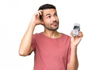 Young handsome caucasian man holding a engagement ring over isolated background having doubts and with confuse face expression
