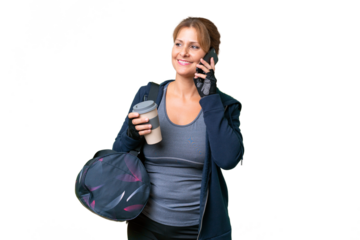 Middle-aged sport woman with sport bag over isolated background holding coffee to take away and a mobile