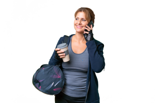 Middle-aged sport woman with sport bag over isolated background holding coffee to take away and a mobile