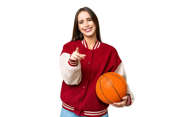 Young beautiful woman playing basketball over isolated chroma key background surprised and pointing...