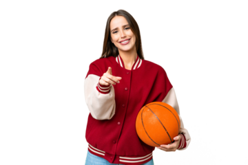 Young beautiful woman playing basketball over isolated chroma key background surprised and pointing front