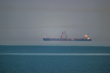 A long ship stands next to the cranes on the sea blue horizon