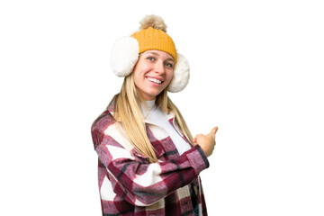 Young pretty blonde woman wearing winter muffs over isolated chroma key background pointing back