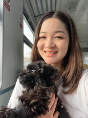 Cute Korean woman holding black poodle puppy in arms and smiling. Traveling with dog. Happy Asian...