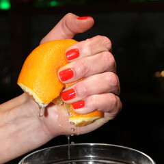 Strong woman's hand with red fingernails squeezing big orange