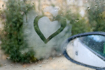Heart drawing on foggy car window with rain drops 