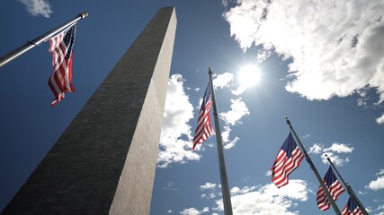 American flags flying outdoors in bright sun at the base of the Washington Monument in Washington,...