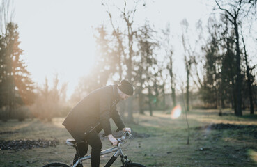 A man is seen riding a bicycle in a tranquil park, surrounded by trees and bathed in soft sunlight,...