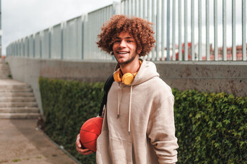 Portrait of male student with curly hair holding a basket ball. Modern hipster man. Street life.