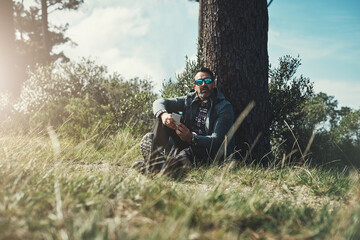 Fototapeta premium Tree, nature and man on ground, smartphone and sunglasses with sunshine, grass and environment. Explore, person and guy with clouds, adventure and journey with vacation, cellphone and getaway trip