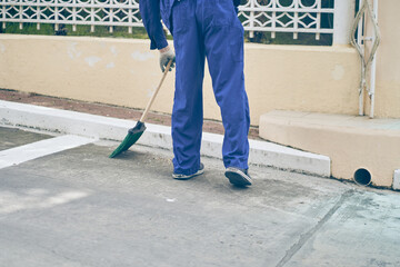 A male janitor sweeps a parking space next to a shopping center with a broom. City cleaning, janitor. High quality photo