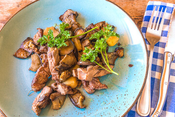 Top view for meat and mushrooms with parsley on a blue plate and fork and knife on a checkered napkin