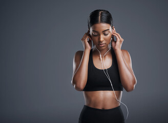 Naklejka premium Woman, fitness and headphones in studio for music, listening and podcast by dark background. Female athlete, streaming and audio for workout, sports training and thinking of playlist on mockup space