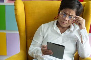 Upset Unhappy Middle aged Asian aunt, aged woman using computer tablet, negative expression, concept image for slow connection, internet scam, internet fraud