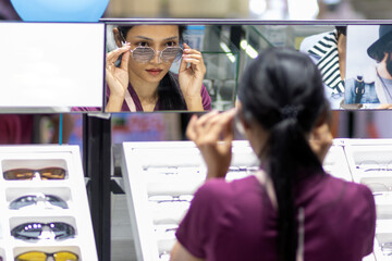 A young woman tries on glasses at the mirror in an optical shop