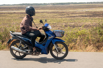 A man rides on a motorcycle at a rural road.