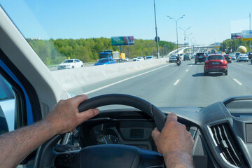 Male hands hold the steering wheel of a car while driving on a highway.