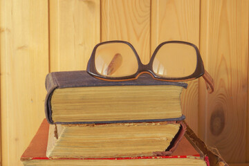 Old glasses with thick lenses lie on old books. The concept of damage to eyesight reading books.