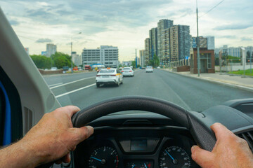 The driver's hands on the steering wheel of a car that is driving around the city.